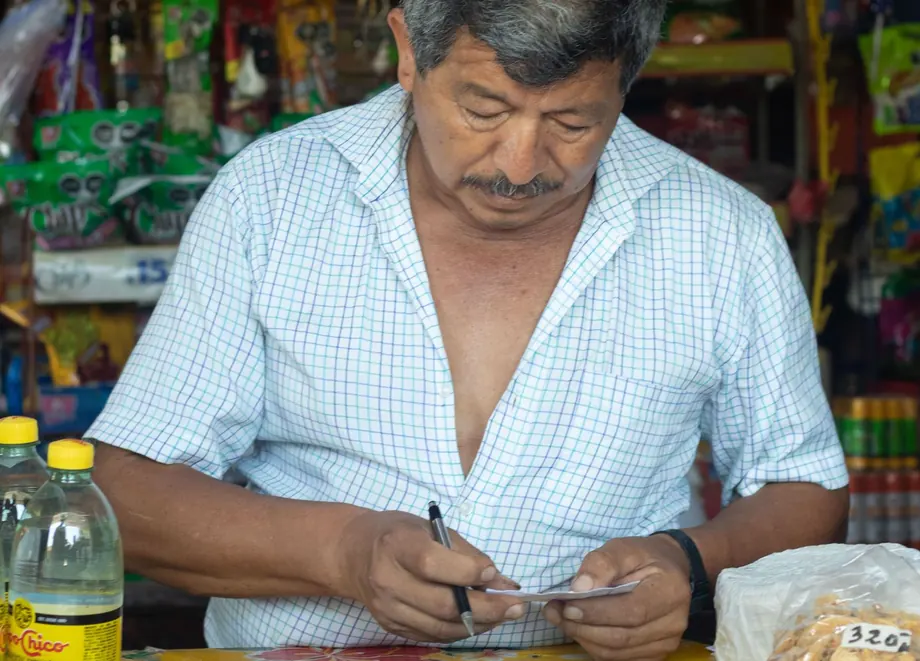 Un comerciante anotando las cuentas a mano detrás del mostrador de su kiosco